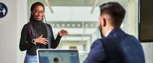 Photograph of a FABSS student speaking to a person sat behind a desk using a laptop.